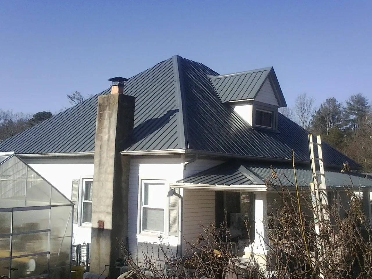 Dark blue standing seam metal roof on a white farmhouse with dormer — Slate & Tile Roof Repair by Roofing Brothers in Jackson Springs