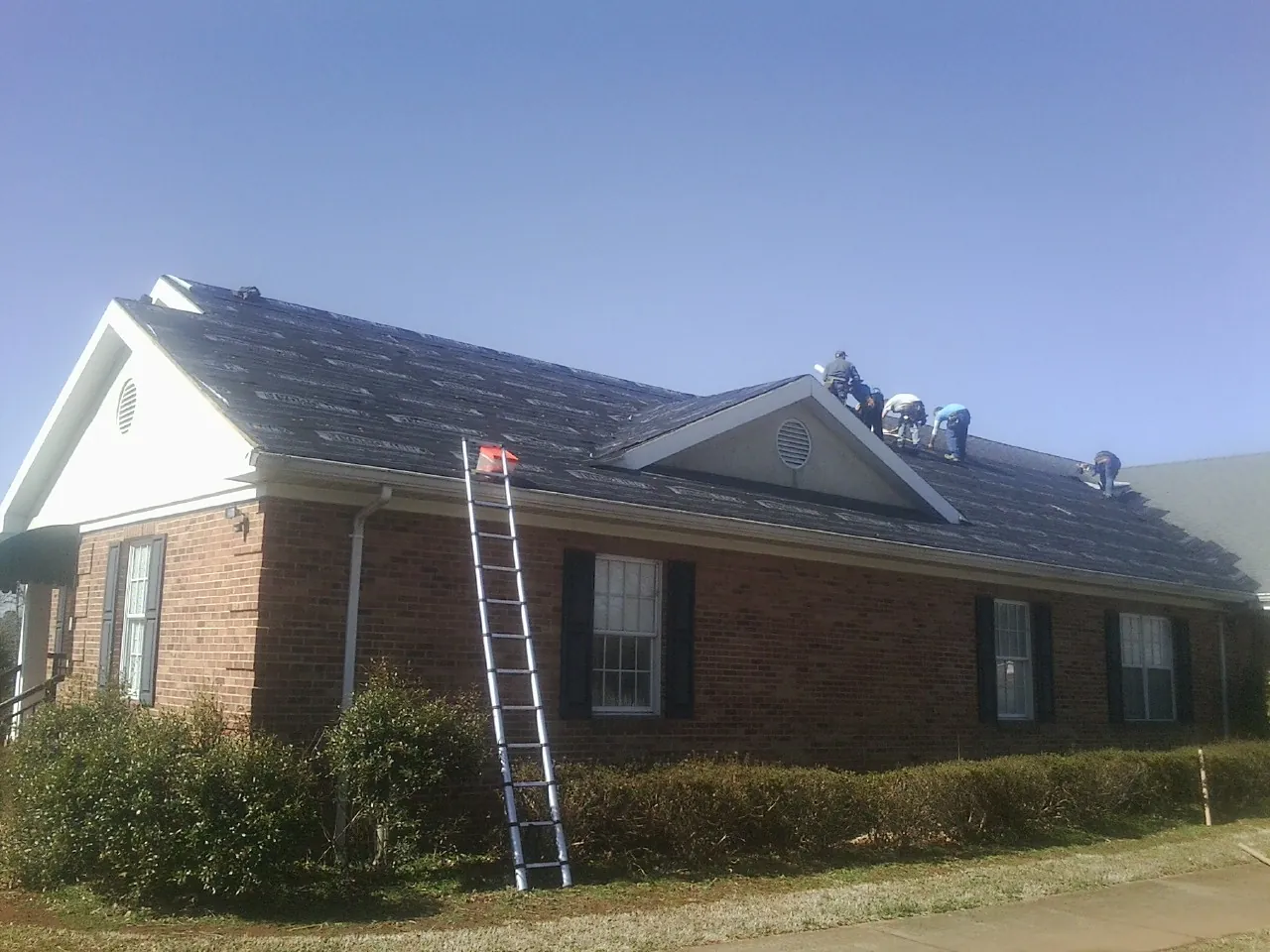 Crew tearing shingles off a brick ranch roof with a ladder set — Emergency Roof Repair work by our crew in Jackson Springs