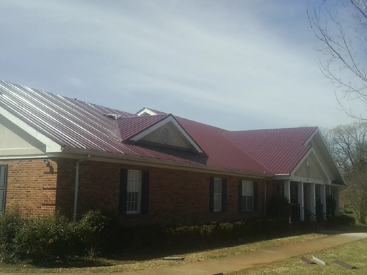 Red metal roof with gabled entries on a long brick building, from a Hail Damage Roof Repair job in Jackson Springs