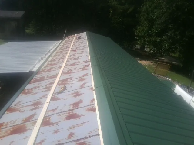 Old rusted panels beside newly installed green metal roofing — Wind Damage Roof Repair by Roofing Brothers in Jackson Springs