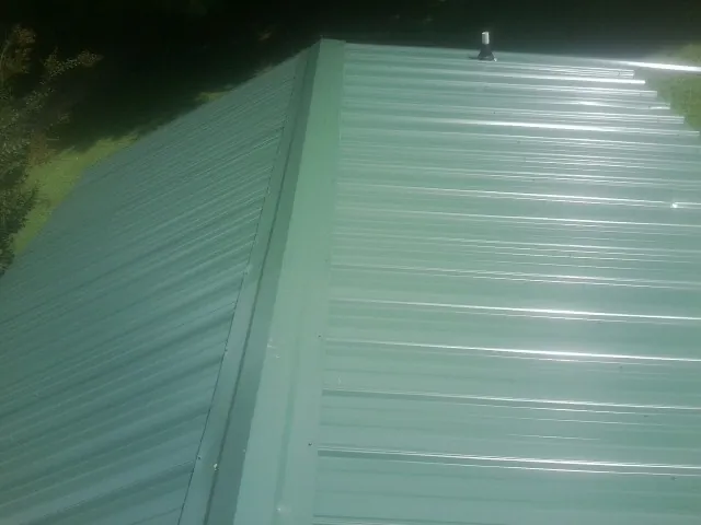 New green metal panels meeting at the ridge of a roof — Flat Roof Repair work by our crew in Jackson Springs
