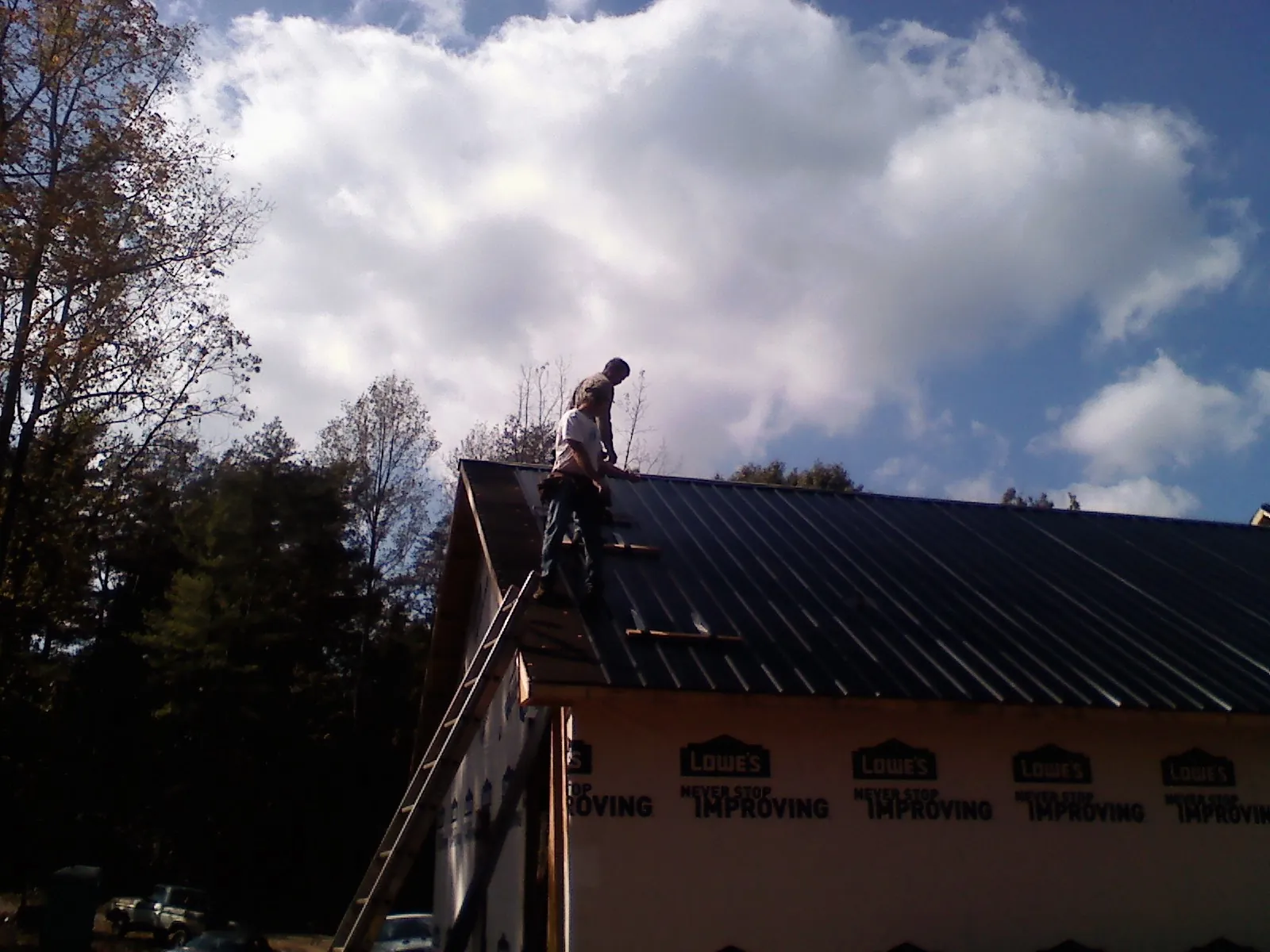 Roofer fastening dark metal panels high against a cloudy sky, from a Roof Inspection job in Jackson Springs