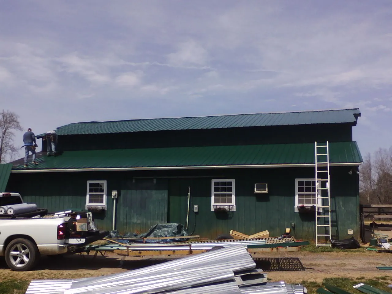 Crew installing green metal roofing on a large green barn in Jackson Springs