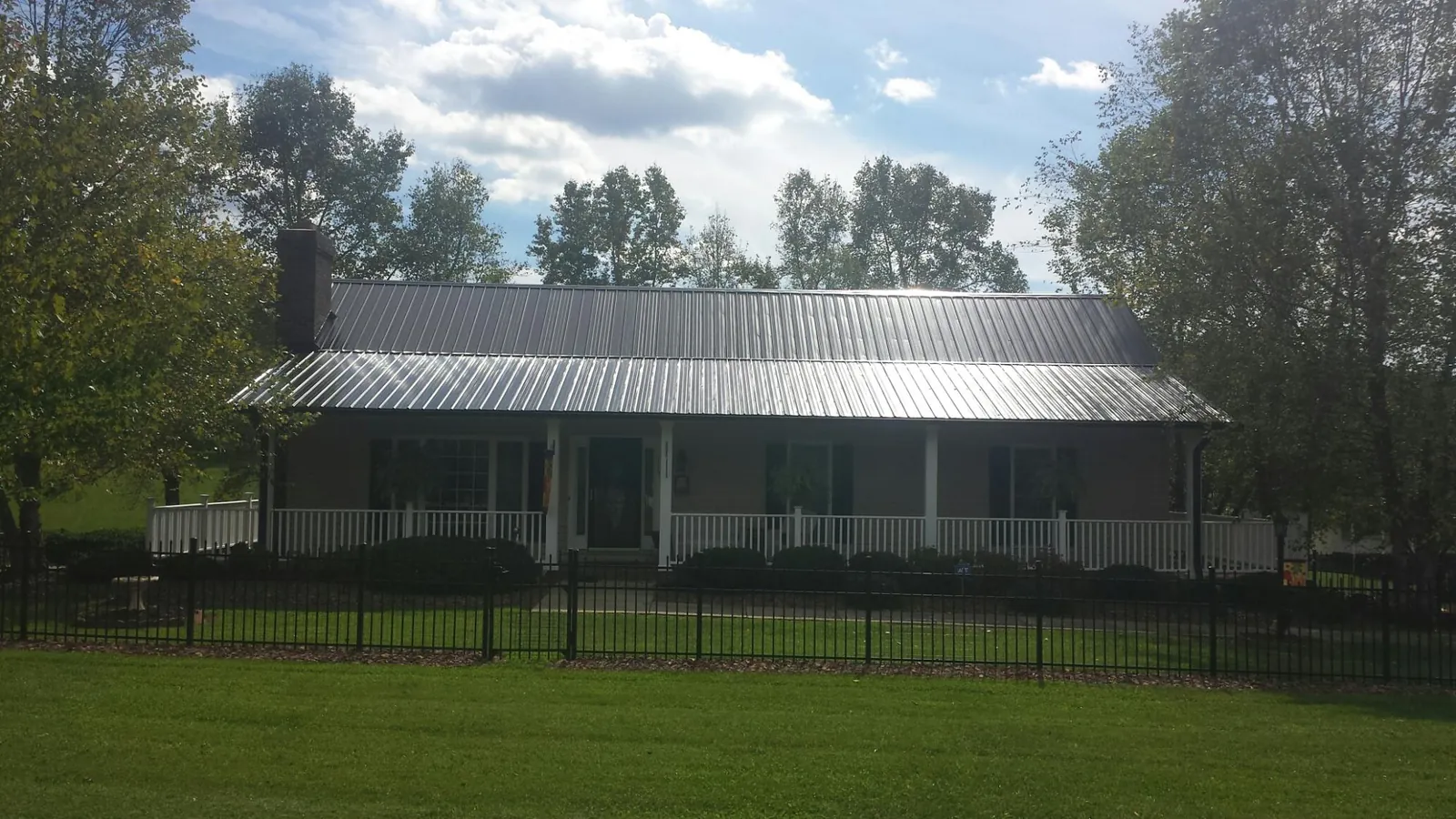 Gray metal roof on a brick ranch with a full width front porch — Gutter Guard Installation work by our crew in Jackson Springs