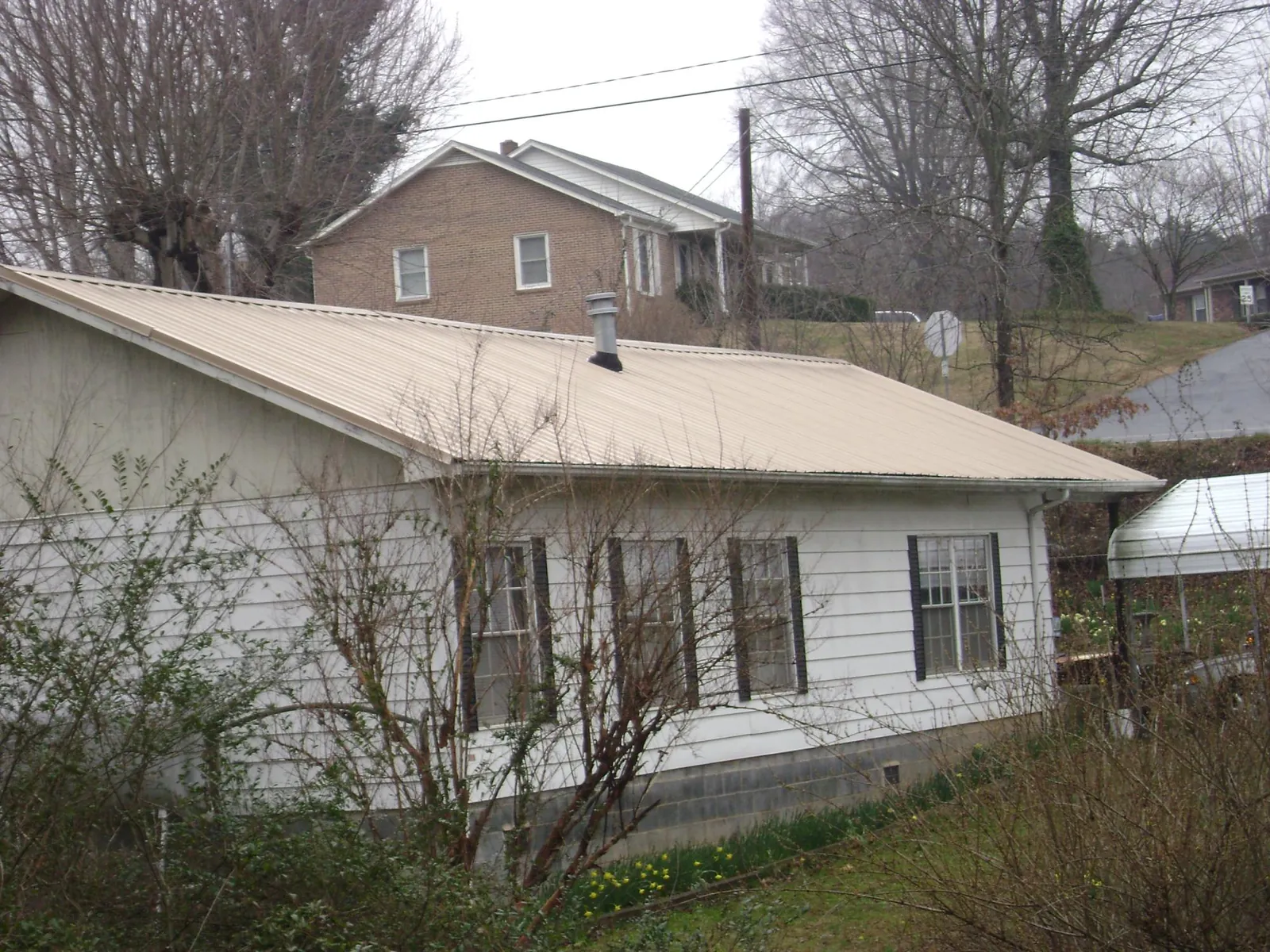Tan metal roof on a white sided house set into a hillside — Commercial Roofing by Roofing Brothers in Jackson Springs