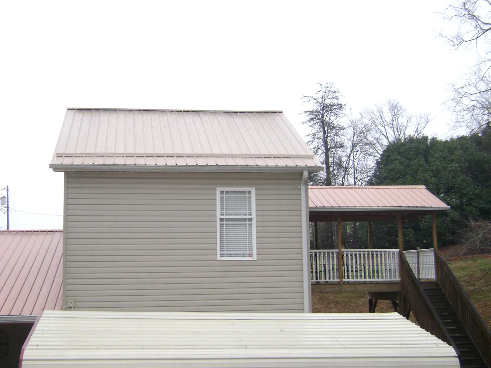 Tan metal roofs on a two story addition and attached porch, from a Roof Replacement job in Jackson Springs